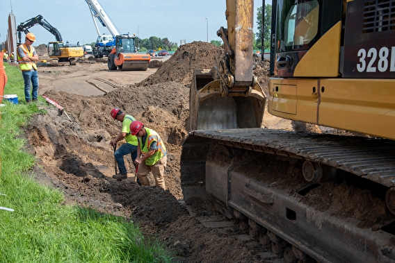 Construction workers standing in a freshly dug hole near equipment